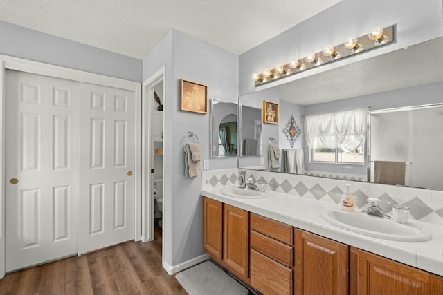 full bath with double vanity, toilet, wood finished floors, and a sink