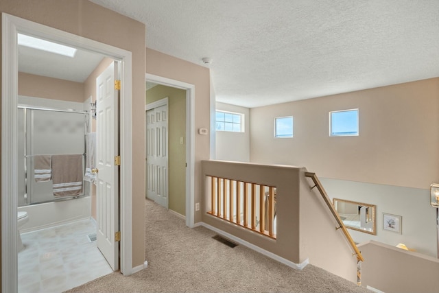 corridor featuring visible vents, an upstairs landing, a textured ceiling, carpet floors, and baseboards