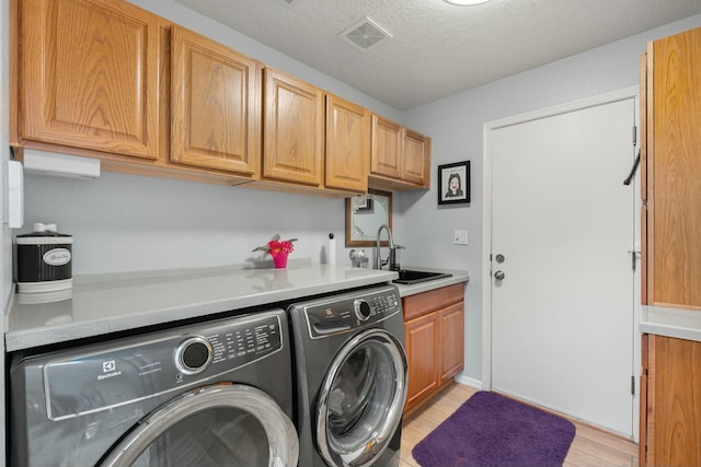 laundry room featuring visible vents, cabinet space, a sink, light wood-style floors, and washer and clothes dryer