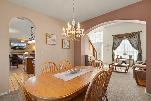 dining space with stairway, light carpet, light tile patterned floors, ceiling fan with notable chandelier, and arched walkways