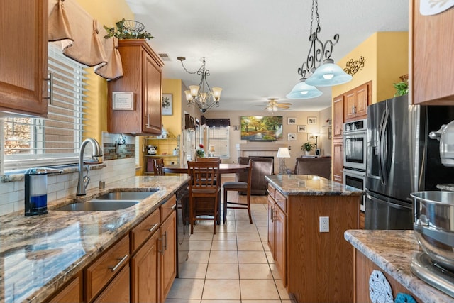 kitchen with ceiling fan with notable chandelier, a sink, tasteful backsplash, appliances with stainless steel finishes, and light tile patterned floors