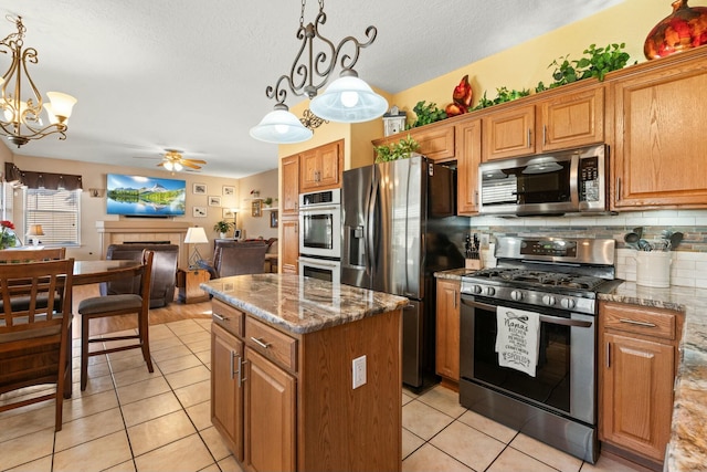 kitchen with tasteful backsplash, a center island, ceiling fan with notable chandelier, appliances with stainless steel finishes, and light tile patterned flooring