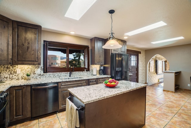 kitchen with black fridge, a sink, a skylight, dark brown cabinets, and dishwasher