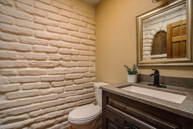 bathroom featuring toilet, vanity, and a textured wall