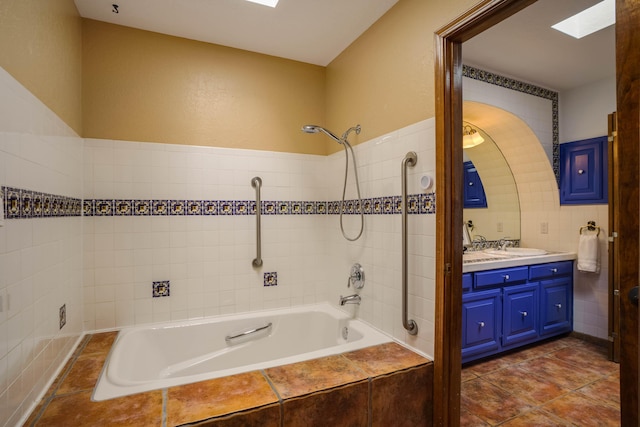 bathroom with a skylight, tile walls, vanity, and tiled shower / bath combo