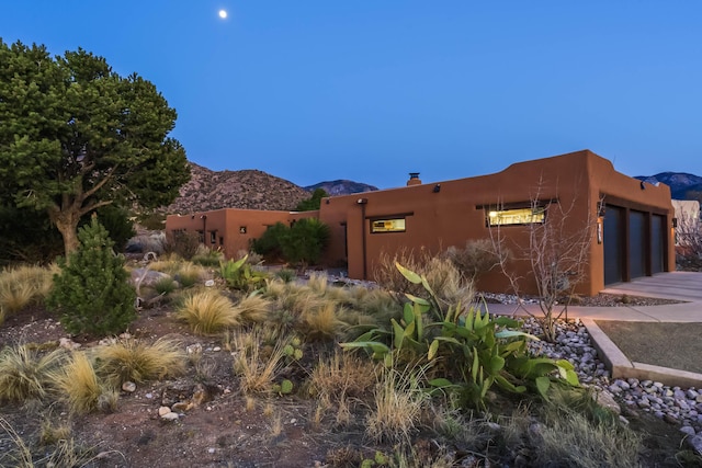 view of side of home featuring concrete driveway, a garage, a mountain view, and a chimney