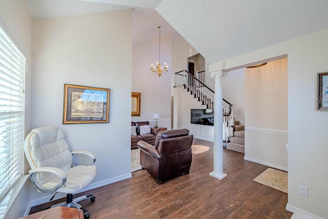 sitting room featuring stairway, wood finished floors, baseboards, ornate columns, and an inviting chandelier