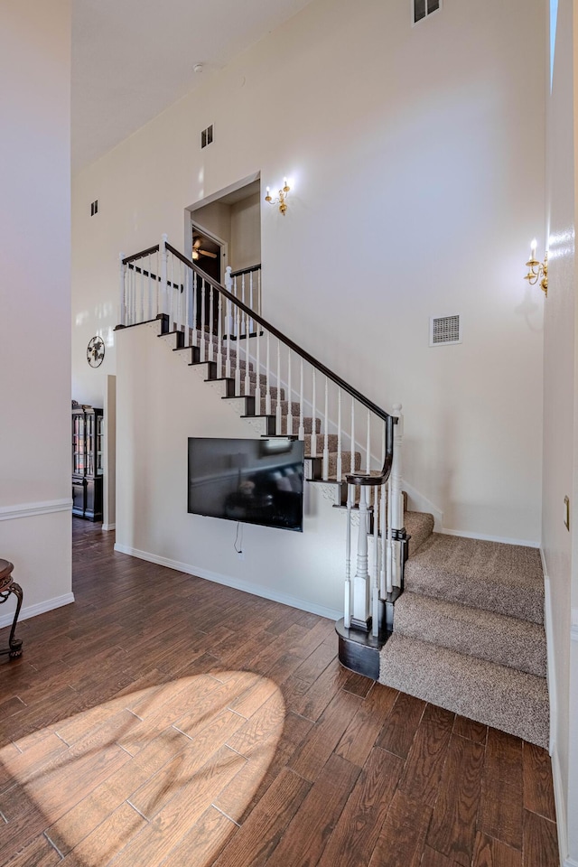 stairway featuring visible vents, wood finished floors, baseboards, and a towering ceiling