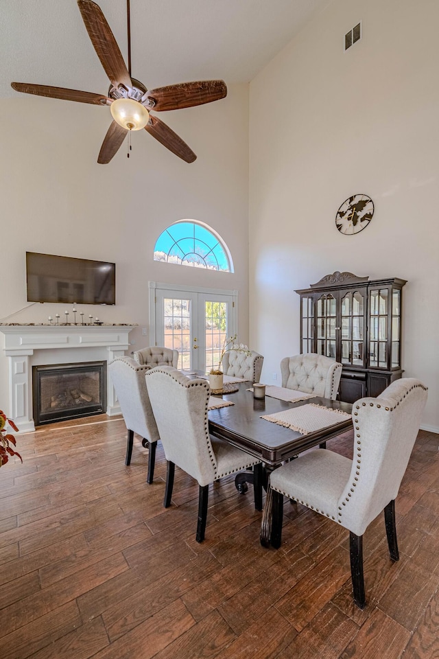 dining room with visible vents, a glass covered fireplace, hardwood / wood-style floors, french doors, and a high ceiling