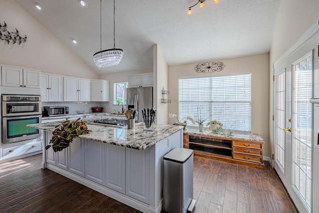 kitchen with light stone counters, stainless steel appliances, white cabinets, dark wood-style flooring, and vaulted ceiling