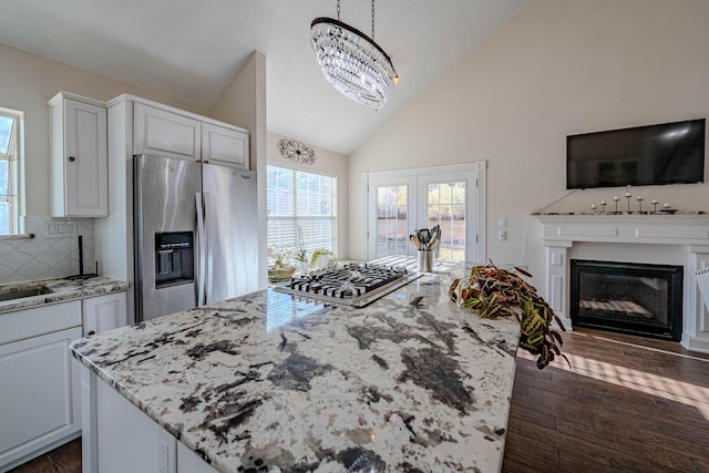 kitchen featuring a glass covered fireplace, lofted ceiling, light stone countertops, and appliances with stainless steel finishes