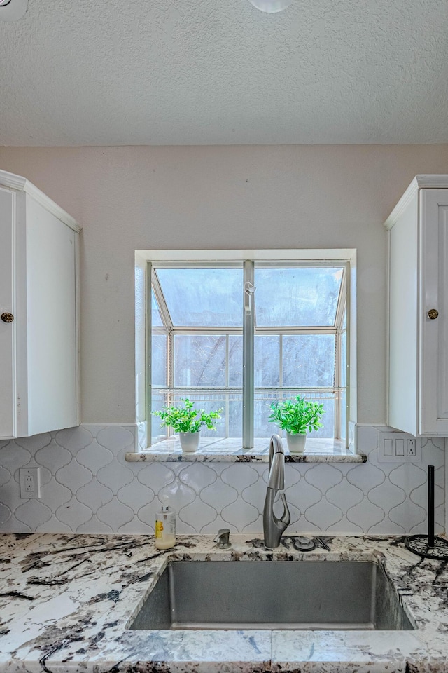 kitchen featuring a sink, tasteful backsplash, white cabinets, and a textured ceiling