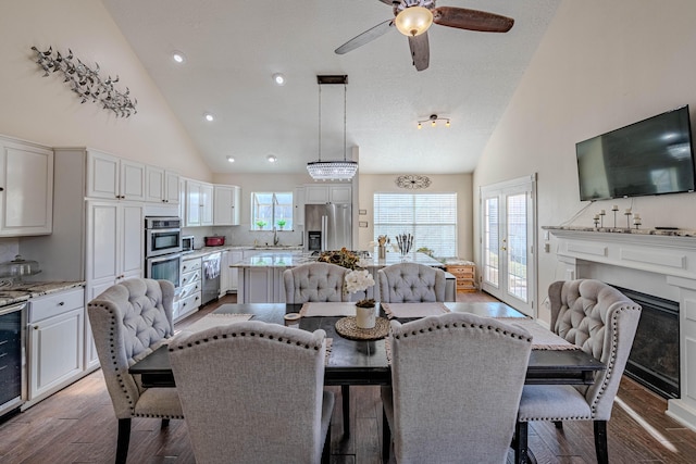 dining space with a glass covered fireplace, wine cooler, high vaulted ceiling, and wood finished floors