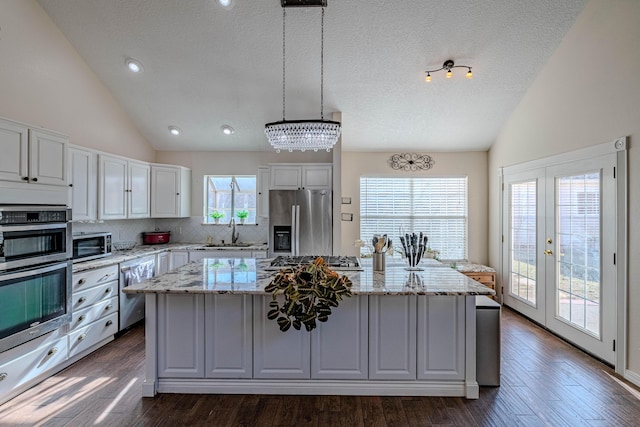 kitchen with a center island, vaulted ceiling, white cabinets, stainless steel appliances, and a sink