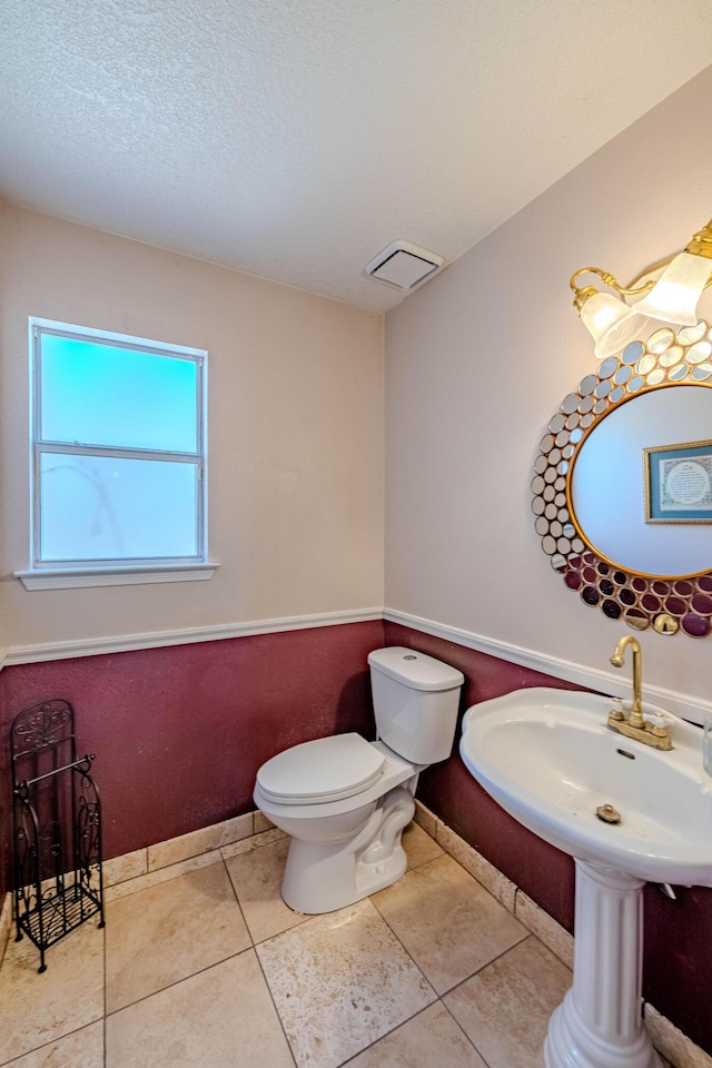 half bath with visible vents, toilet, tile patterned flooring, and a textured ceiling