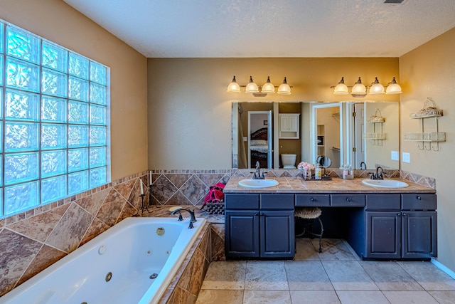 ensuite bathroom with a textured ceiling, a jetted tub, ensuite bathroom, and a sink