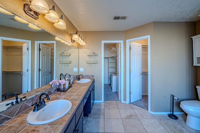 bathroom featuring visible vents, a textured ceiling, toilet, and a sink