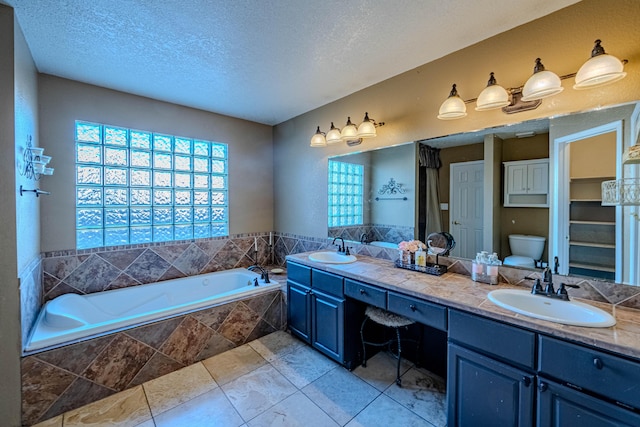 bathroom with a textured ceiling, toilet, a garden tub, and a sink