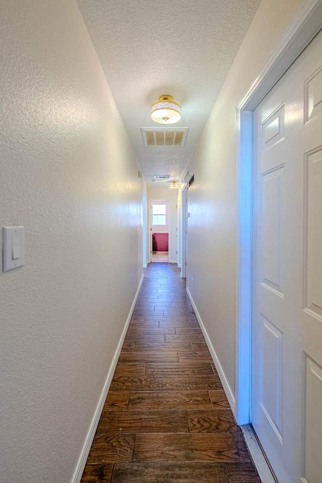 hall with dark wood-type flooring, baseboards, visible vents, and a textured ceiling