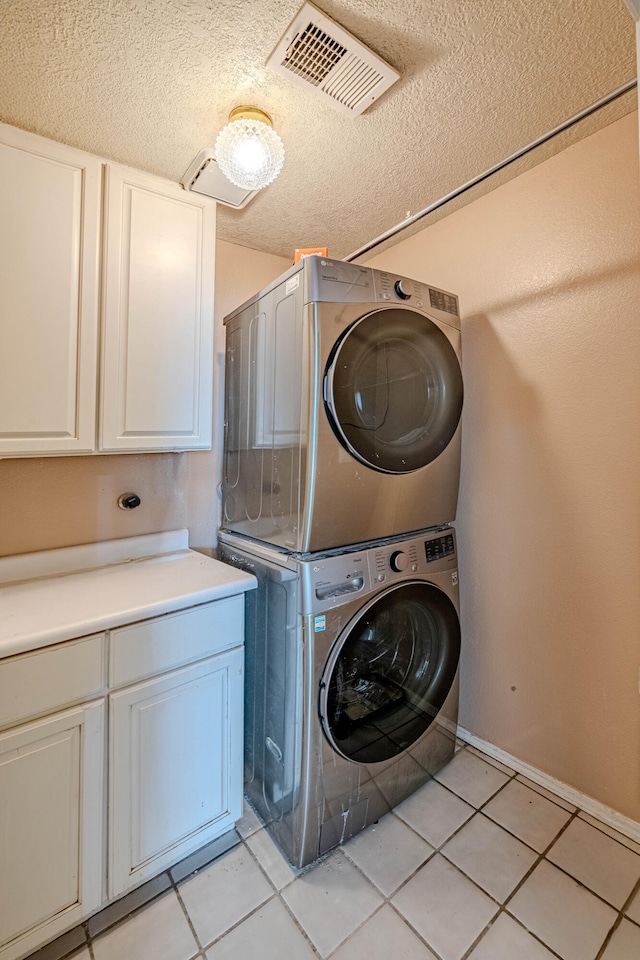 laundry area featuring visible vents, stacked washer and dryer, a textured ceiling, cabinet space, and light tile patterned floors