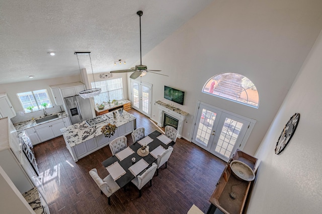 living room with high vaulted ceiling, a textured ceiling, a glass covered fireplace, dark wood-style floors, and french doors