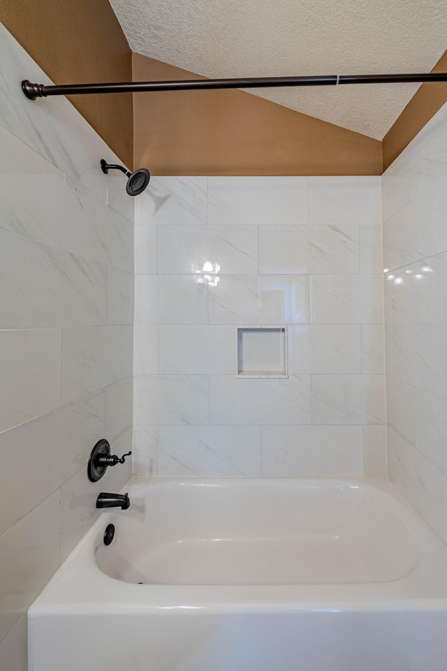 bathroom with vaulted ceiling, tub / shower combination, and a textured ceiling