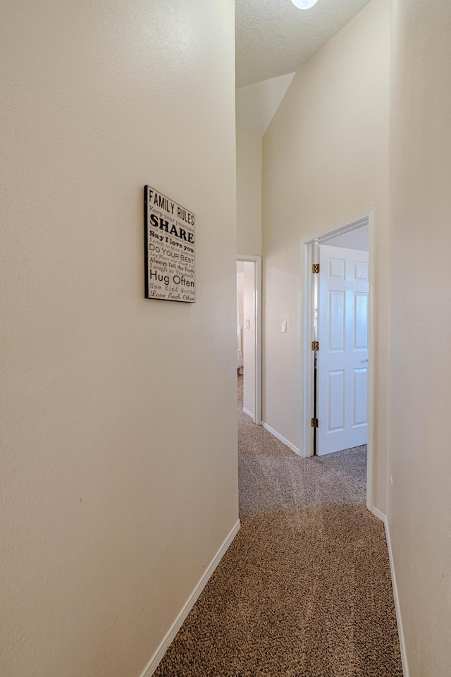 hallway with baseboards, carpet floors, and high vaulted ceiling