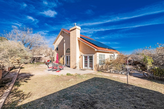 back of house with solar panels, a chimney, stucco siding, french doors, and a patio area