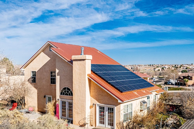 rear view of property featuring roof mounted solar panels, stucco siding, french doors, a chimney, and metal roof