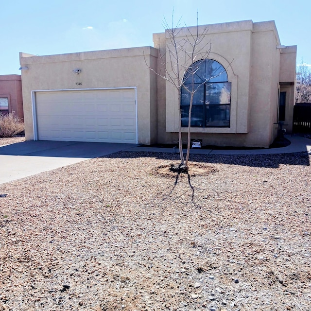 pueblo-style home featuring concrete driveway, an attached garage, and stucco siding