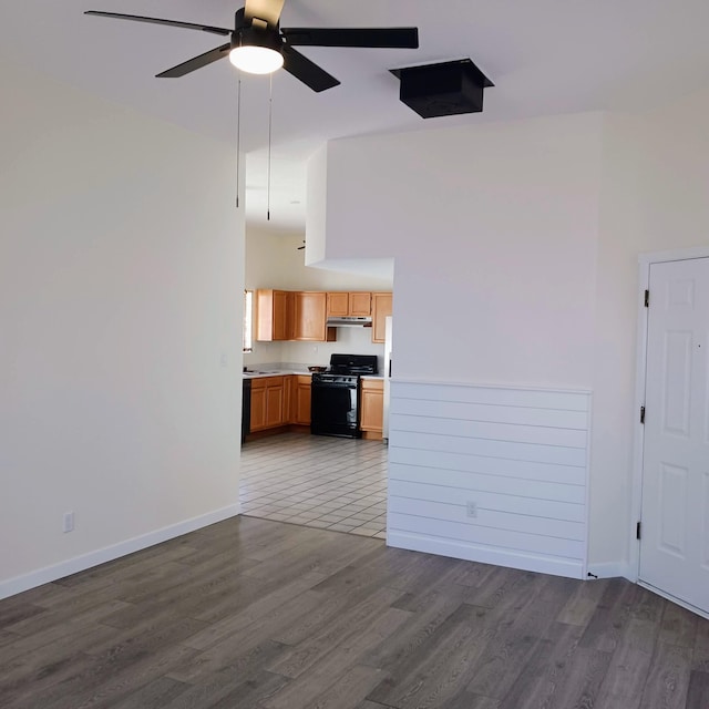 unfurnished living room featuring dark wood-style floors, ceiling fan, baseboards, and a towering ceiling