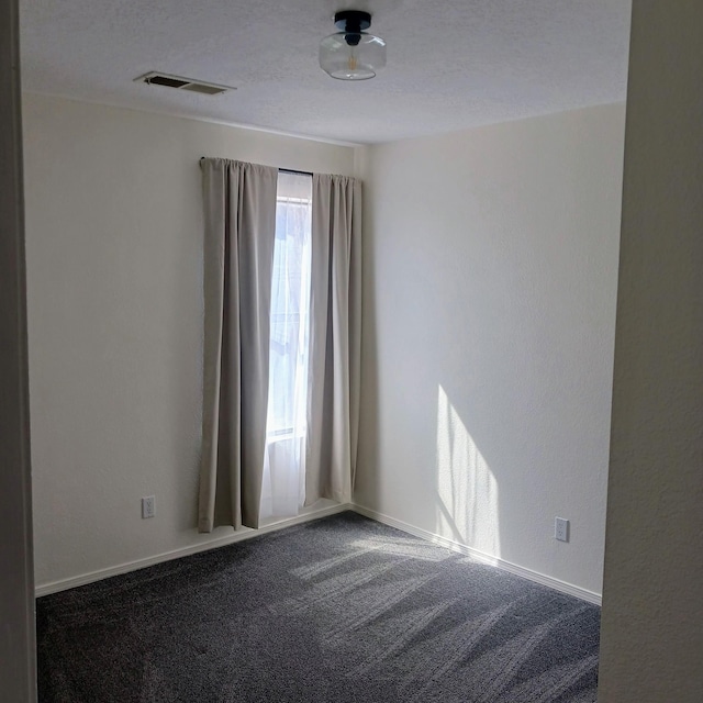 carpeted spare room with baseboards, visible vents, and a textured ceiling