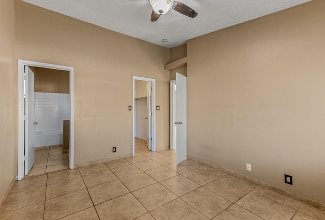 unfurnished bedroom featuring connected bathroom, a walk in closet, ceiling fan, light tile patterned flooring, and a textured ceiling