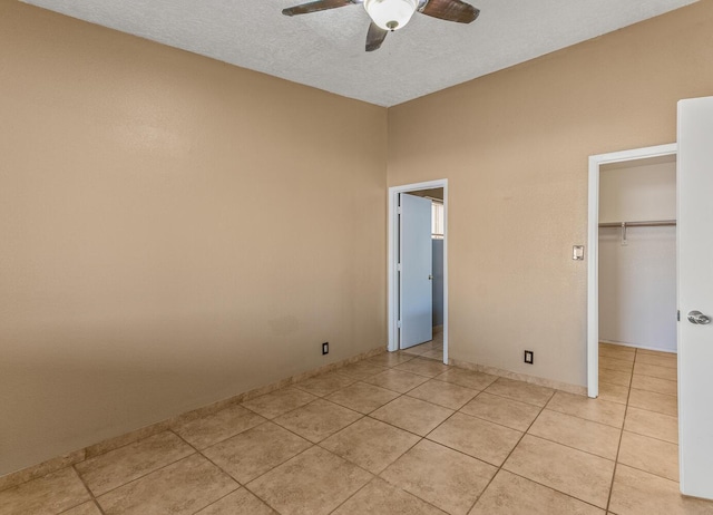 unfurnished bedroom featuring a walk in closet, a textured ceiling, a closet, light tile patterned floors, and ceiling fan