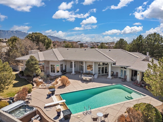 rear view of property with a mountain view, french doors, a hot tub, and a tile roof