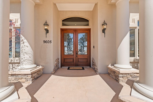 view of exterior entry with stucco siding, stone siding, a porch, and french doors