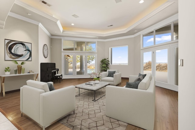 living room with a tray ceiling, visible vents, light wood-style floors, and crown molding