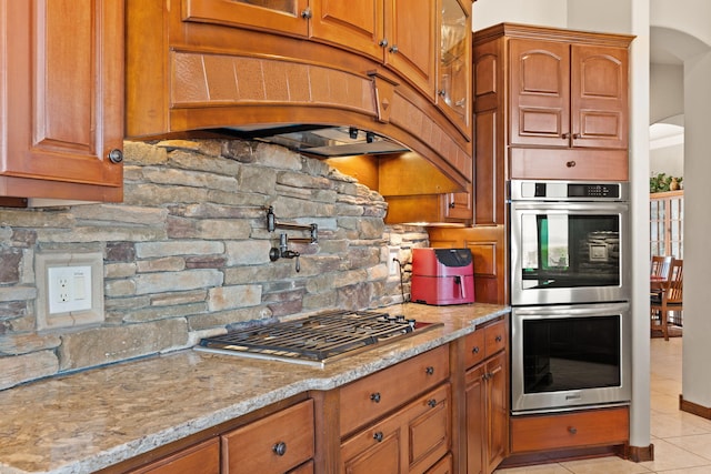 kitchen with brown cabinetry, stainless steel appliances, and light stone counters