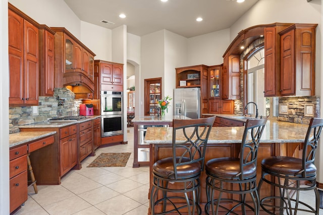 kitchen featuring a kitchen bar, light stone counters, stainless steel appliances, arched walkways, and a peninsula