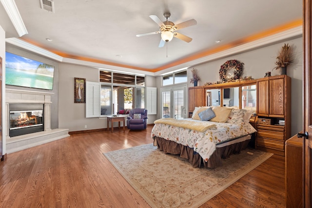 bedroom featuring visible vents, crown molding, baseboards, wood finished floors, and a glass covered fireplace