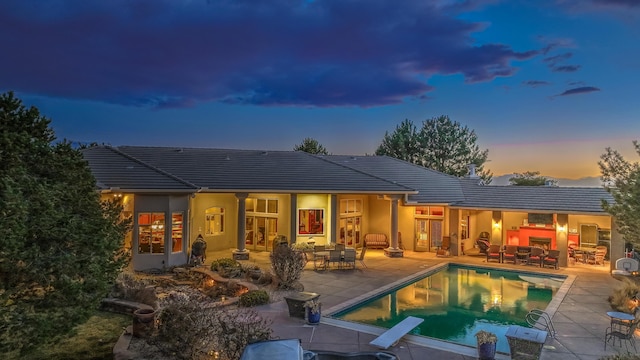 back of property with a tiled roof, a patio area, an outdoor pool, and stucco siding