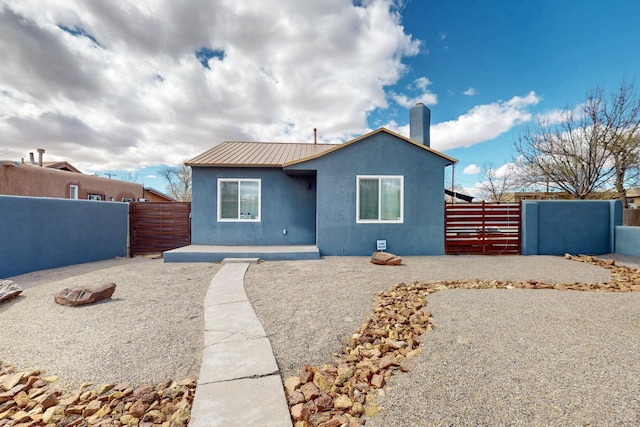 bungalow featuring stucco siding, metal roof, a chimney, and fence