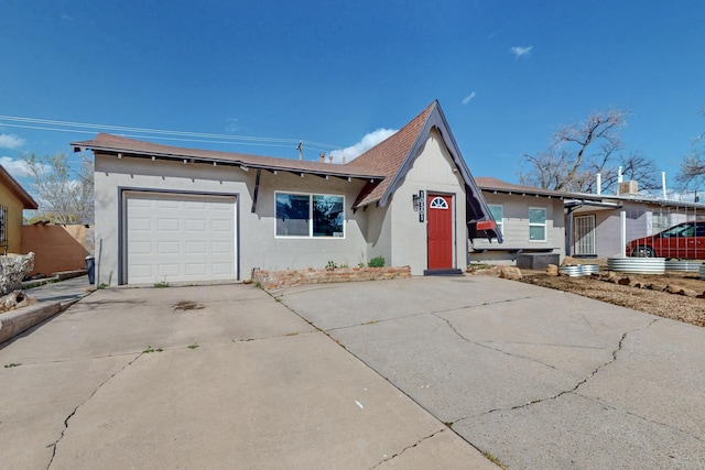 a-frame home with stucco siding, roof with shingles, concrete driveway, and an attached garage