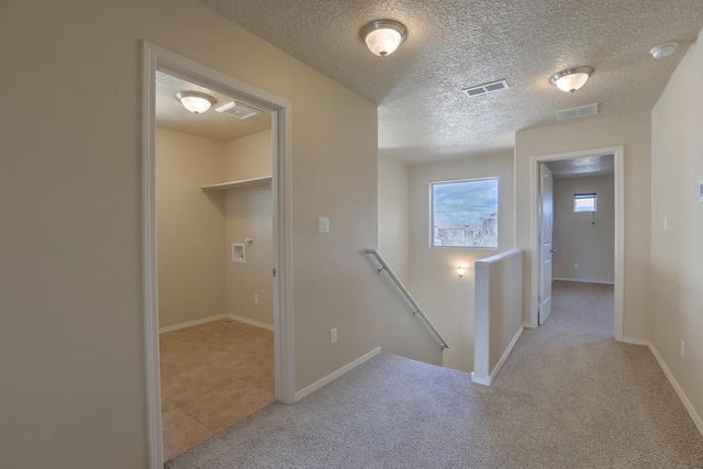 hallway with an upstairs landing, visible vents, carpet flooring, and a textured ceiling