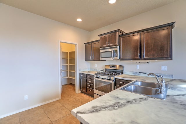 kitchen featuring a sink, dark brown cabinetry, appliances with stainless steel finishes, light countertops, and light tile patterned floors