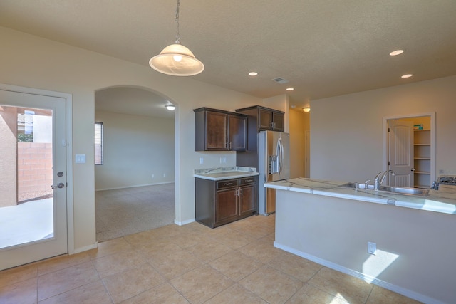 kitchen featuring dark brown cabinetry, light countertops, stainless steel refrigerator with ice dispenser, arched walkways, and a sink