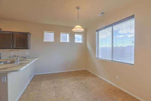 unfurnished dining area featuring visible vents, baseboards, light tile patterned floors, a textured ceiling, and a sink