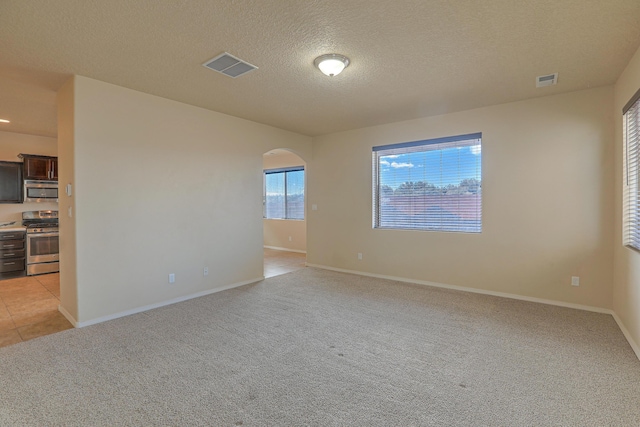 spare room with a textured ceiling, light colored carpet, visible vents, and arched walkways