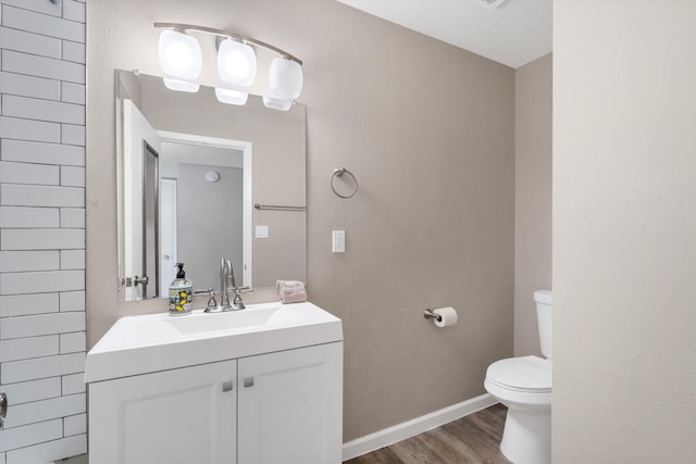 bathroom with toilet, wood finished floors, baseboards, vanity, and a textured wall