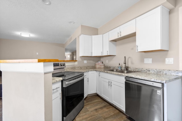 kitchen with dark wood-style floors, a peninsula, a sink, white cabinets, and appliances with stainless steel finishes